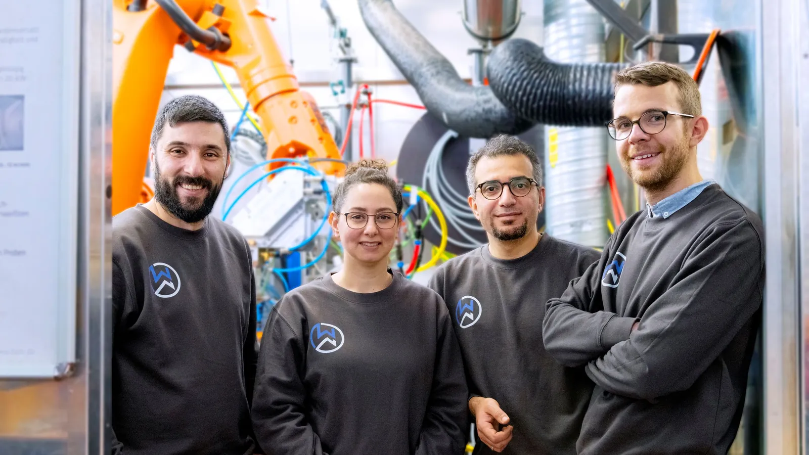 The four members of the WeldNova team in front of a robotic welding cell